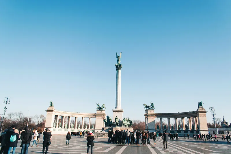 a group of people in a plaza with a column and a statue 
