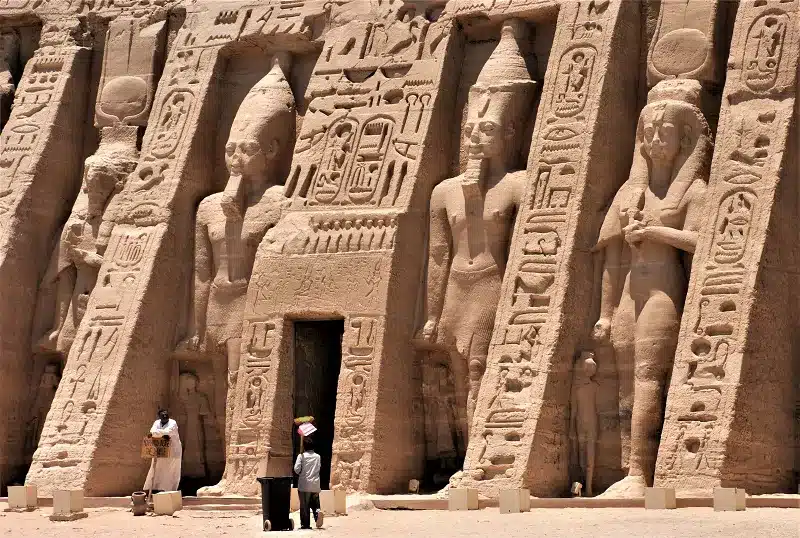 Egyptian landmarks while a group of people standing in front of a stone wall with carvingshot 