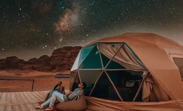 Two people comfortably sitting in a tent, enjoying the peacefulness of a star-filled sky during a camping experience. while their Jordan itinerary 6 days