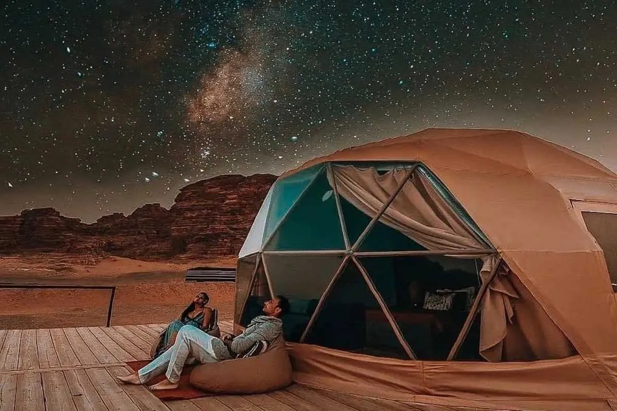 Two people comfortably sitting in a tent, enjoying the peacefulness of a star-filled sky during a camping experience. while their Jordan itinerary 6 days