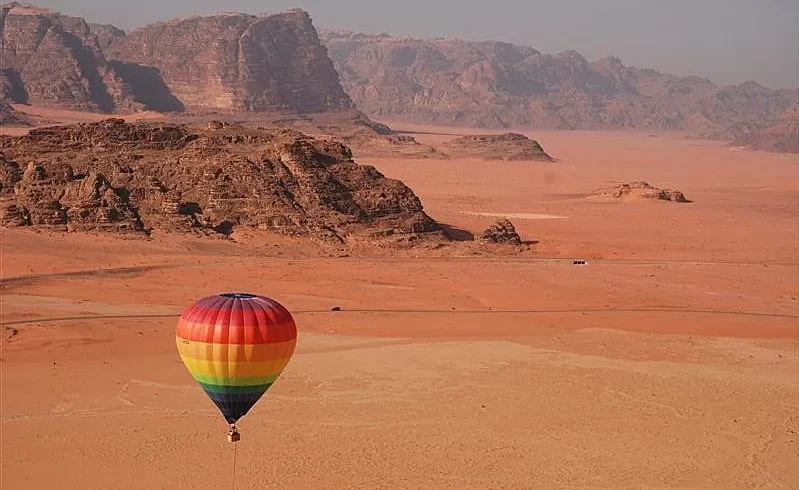 1. A vibrant hot air balloon soars above the vast desert landscape, showcasing the beauty of the arid terrain below while our Jordan itinerary 8 days