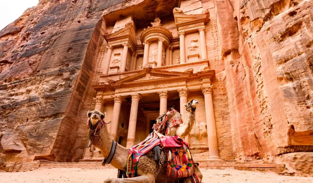 A camel rests at the entrance of Petra's Treasury, showcasing the ancient architecture and desert landscape in Jordan itinerary 7 days